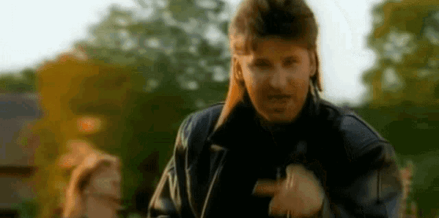 a man in a leather jacket is dancing in front of a woman in a park .