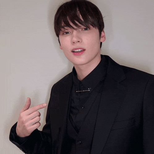 a young man wearing a black suit and a black shirt is pointing at something