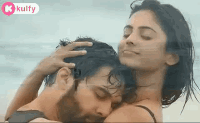 a man and a woman are hugging each other on the beach and the woman is touching the man 's head .