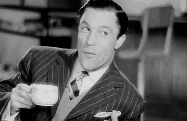 a man in a suit and tie is holding a cup of coffee in his hand .