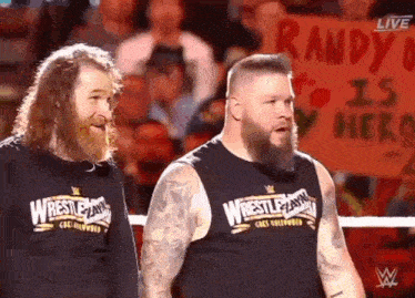 two men are standing next to each other in a wrestling ring with a sign that says randy is my hero .