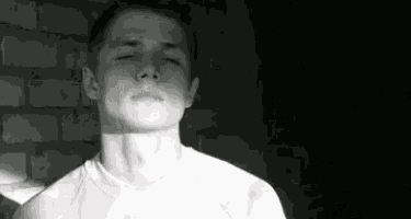 a black and white photo of a young man standing in front of a brick wall .