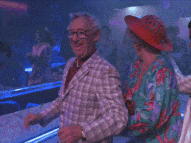 a man in a plaid jacket and a woman in a red hat are dancing in a club