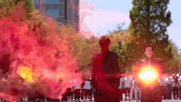 a group of people are standing in front of a large explosion .