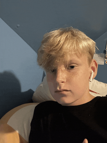 a young boy wearing a black shirt and white ear buds looks at the camera