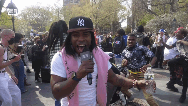 a man wearing a ny hat is holding a microphone in a crowd