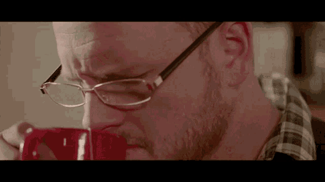 a man wearing glasses is drinking a cup of coffee