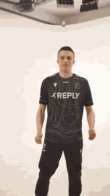 a man wearing a reply shirt stands in front of a white background
