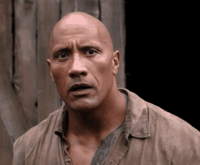 a bald man with a tattoo on his chest looks at the camera with a surprised look on his face