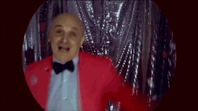 a bald man in a red suit and bow tie is dancing