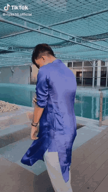 a young man in a blue shirt and white pants is standing in front of a pool ..