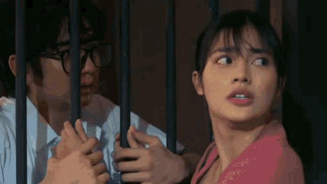 a man and a woman are behind bars and the woman is looking at the man .