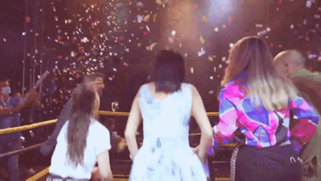 a woman in a white dress is standing in a crowd watching confetti fall