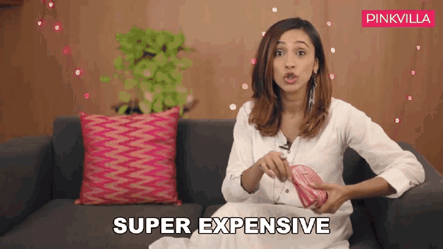 a woman is sitting on a couch and holding a pink purse and says super expensive