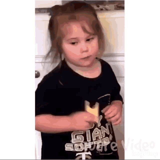 a little girl wearing a black shirt with the word giant on it is standing in front of a door .