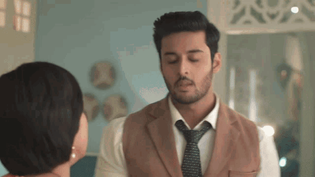 a man in a suit and tie talks to a woman in a room