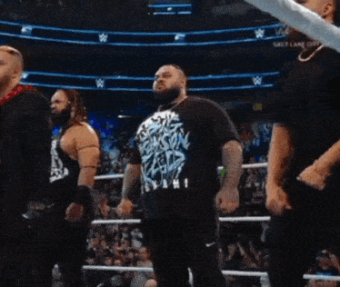a man in a shirt that says ' smackdown ' on it stands in a wrestling ring