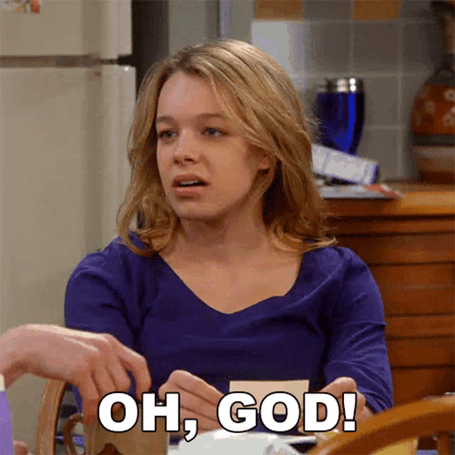 a woman in a blue shirt is sitting at a table with the words oh god written above her