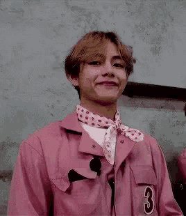 a young man wearing a pink jacket and polka dot scarf is smiling .