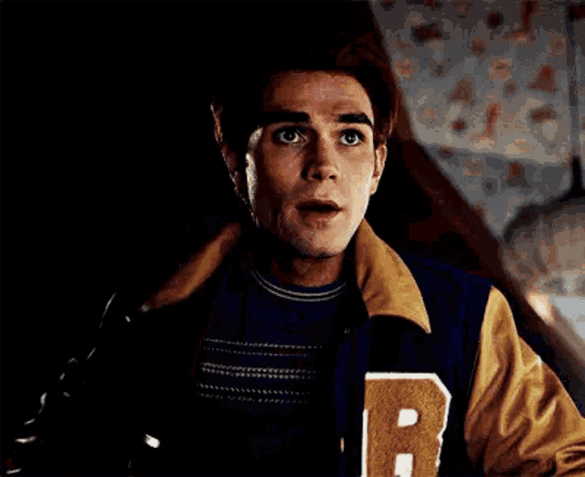 a man with red hair and a surprised look on his face is wearing a jacket .