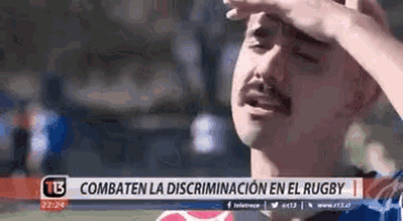 a man with a mustache is covering his face with his hand while watching a rugby game