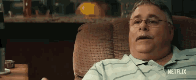 a man with glasses and a mustache is sitting in a chair with a netflix logo behind him