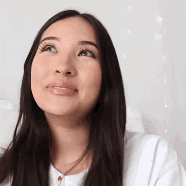a woman with long black hair is wearing a white shirt and a necklace .