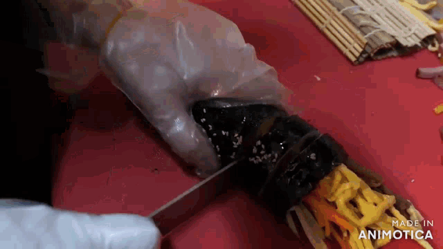 a person is cutting a sushi roll with a knife on a red cutting board .