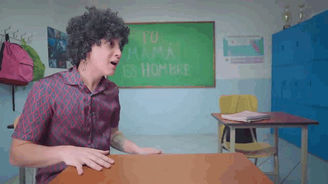 a man sits at a desk in front of a chalkboard that says " tu mama es hombre "