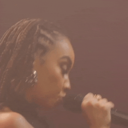 a close up of a woman singing into a microphone while wearing earrings