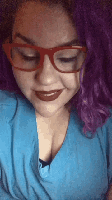 a woman with purple hair and red glasses smiles
