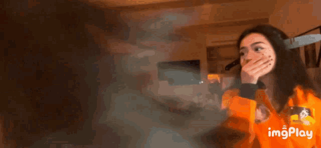 a woman in an orange jacket is covering her mouth with her hand while a knife is stuck to her face