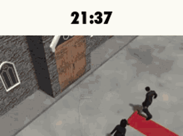 a couple of people carrying a red carpet in front of a building at 21:37