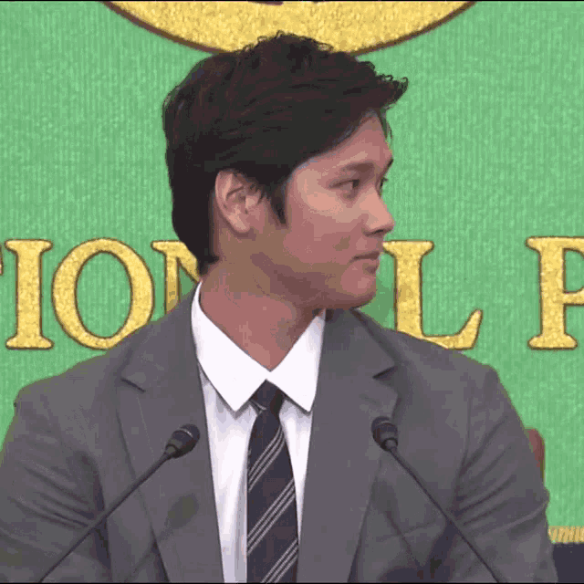 a man in a suit and tie is speaking into a microphone in front of a sign that says " ion "