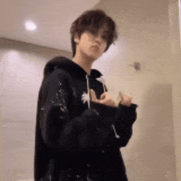 a young man in a black hoodie is standing in a bathroom and making a funny face .