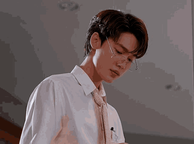 a man wearing glasses and a tie looks down at something