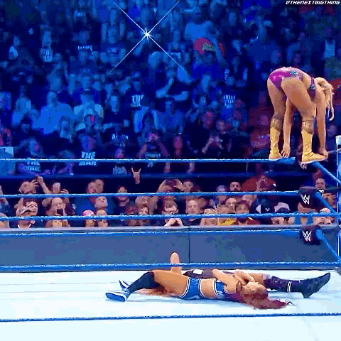 a woman in a pink bikini is jumping over a man in a wrestling ring .