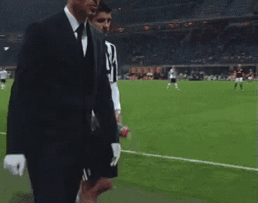 a man in a suit and tie is walking on a soccer field with a bottle of soda in his hand .