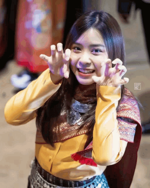 a girl wearing a yellow shirt is making a claw face