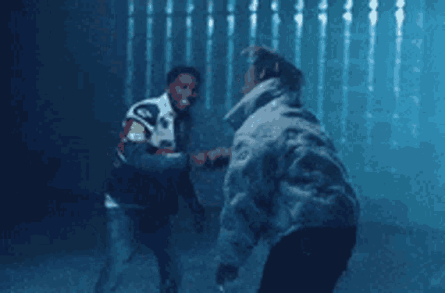 two men are standing next to each other in a dark room and shaking hands .