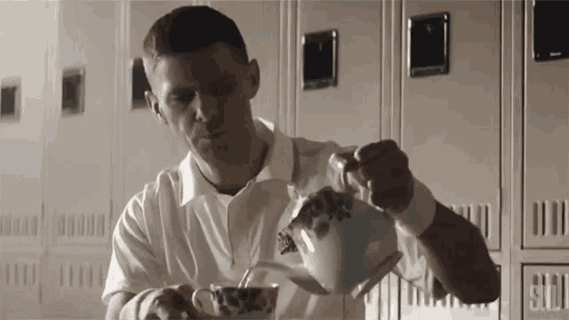 a man pouring tea into a cup in front of a row of lockers that say ' g.i.d. '