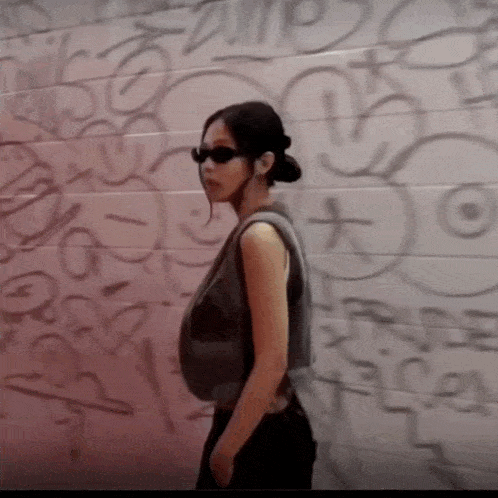 a woman standing in front of a wall with graffiti on it