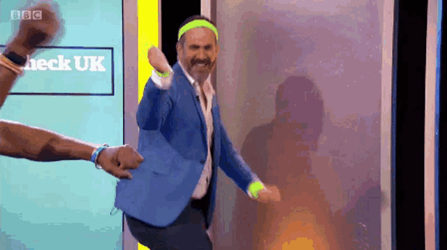 a man in a blue suit is dancing in front of a screen that says check uk