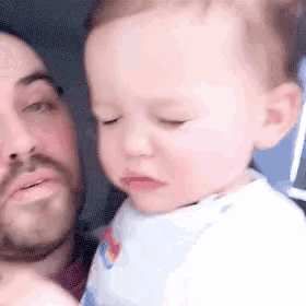 a man is holding a baby in his arms and the baby is making a funny face .