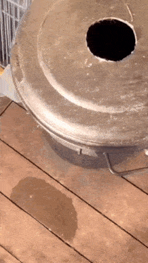 a dirty trash can with a hole in the lid is on a wooden floor .