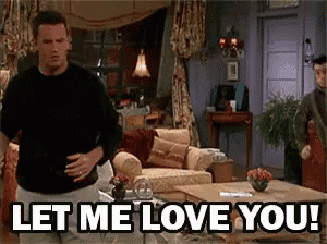 a man is standing in a living room with the words let me love you written on the screen .