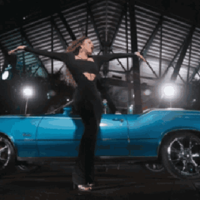 a woman in a black dress stands in front of a blue convertible