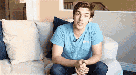 a man in a blue shirt is sitting on a couch with his hands folded