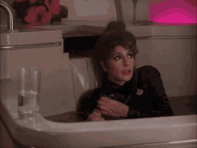 a woman is sitting in a sink with a glass of water