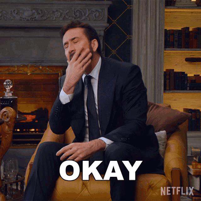 a man in a suit and tie is sitting in a chair with the word okay written in white